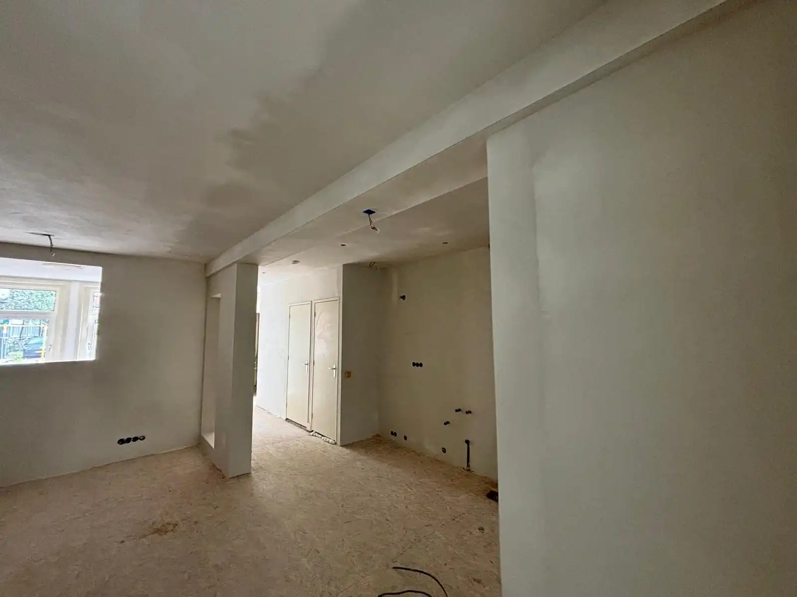 Open ruimte in renovatie met strak gestucte wanden, plafond en doorgang.