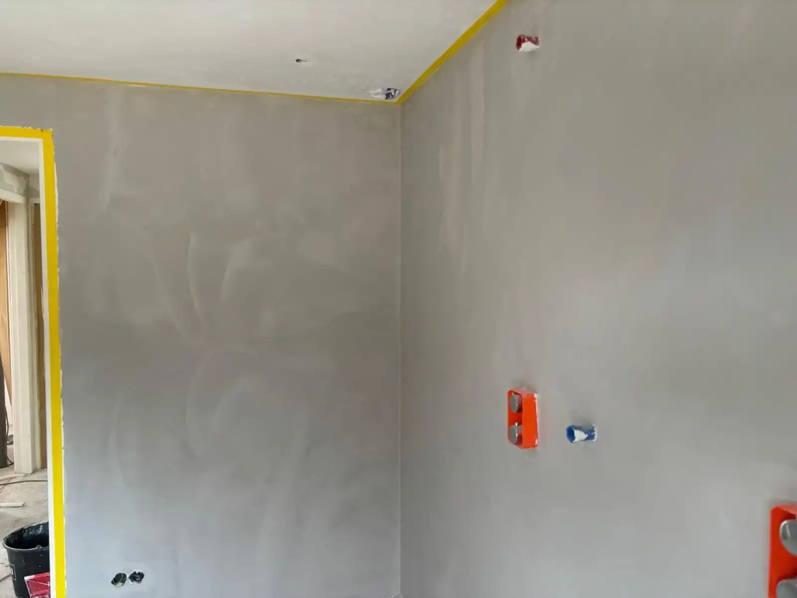 Rechte binnenhoek met vers stucwerk en gele afplaktape langs het plafond.