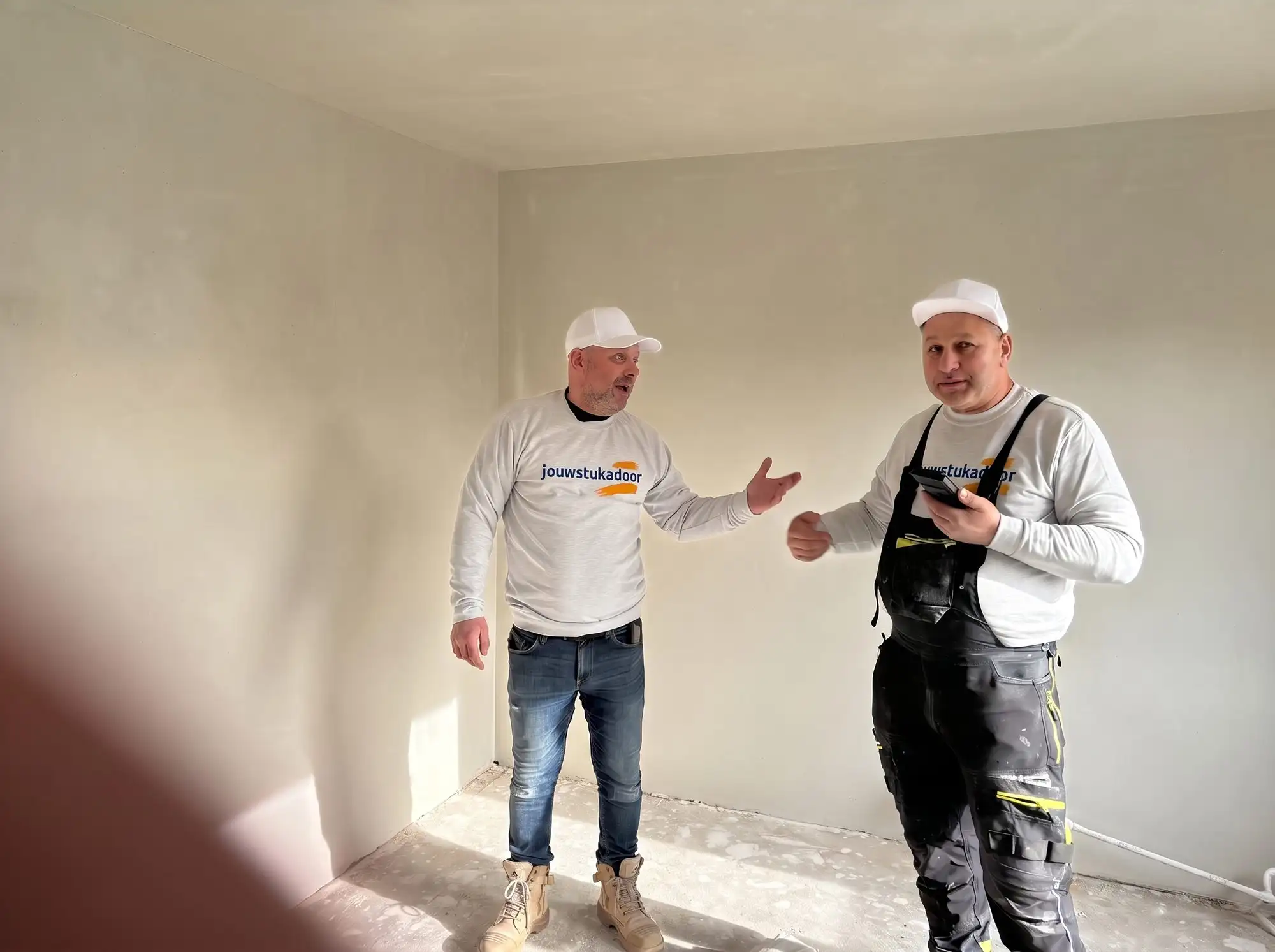 Twee stukadoors van jouwstukadoor overleggen in een gestucte ruimte.